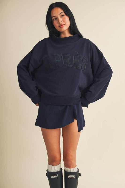 Model wearing oversized navy mock neck sweatshirt with embroidered Après lettering paired with matching shorts