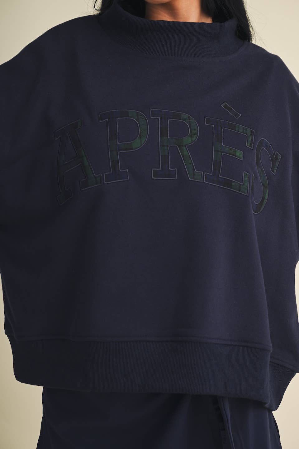 Close-up of oversized mock neck sweatshirt with arched APRÈS lettering in plaid appliqué
