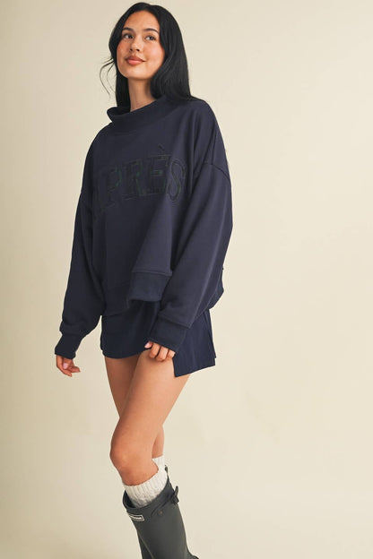 Model wearing oversized navy mock neck sweatshirt with Après lettering, paired with shorts and tall boots