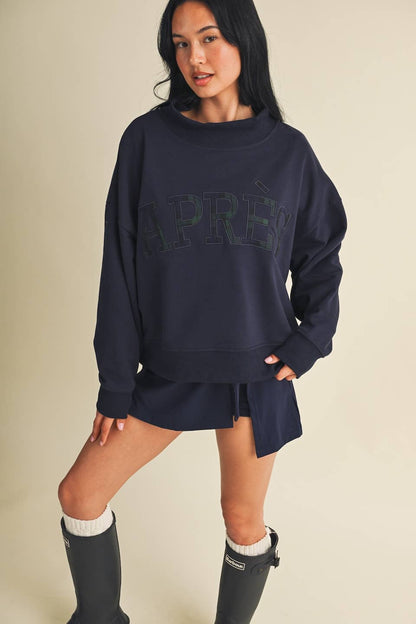 Model wearing oversized mock neck sweatshirt with Après lettering, paired with matching navy shorts and rain boots