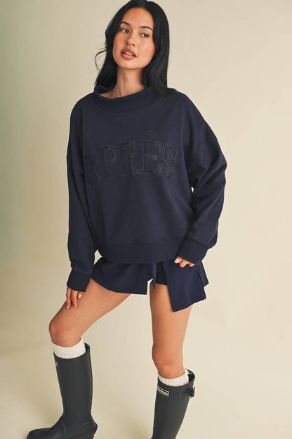 Model wearing oversized navy mock neck sweatshirt with Après lettering, styled with mini skirt and tall rain boots