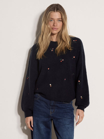 Model wearing a navy fisherman knit jumper with scattered mini embroidered floral details