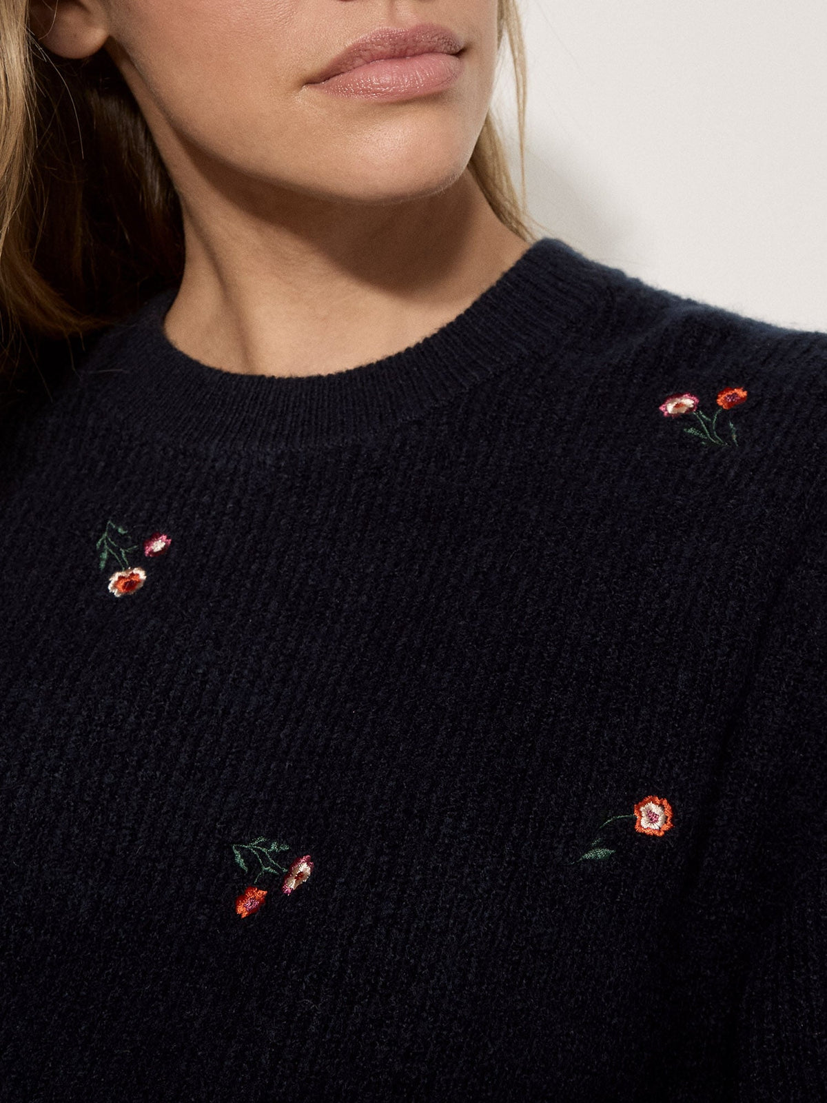 Close-up detail of navy knit jumper featuring scattered red and pink embroidered floral motifs