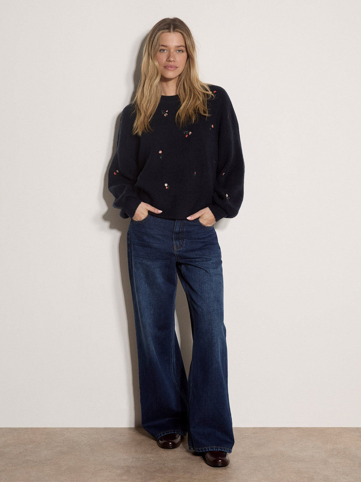 Model wearing a navy knit jumper with delicate floral embroidery and wide-leg jeans
