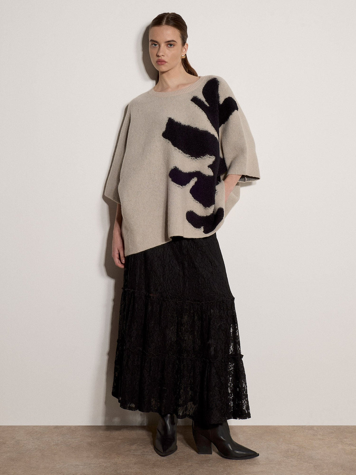 Model wearing oversized stone knit cape jumper with bold abstract black floral intarsia pattern