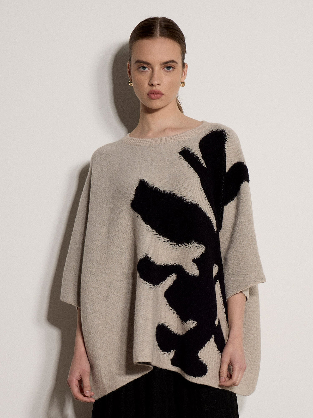 Model wearing oversized knit cape jumper with bold abstract black floral intarsia pattern