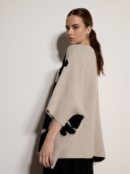 Model wearing oversized knit cape jumper with bold black floral pattern, three-quarter sleeves, side view