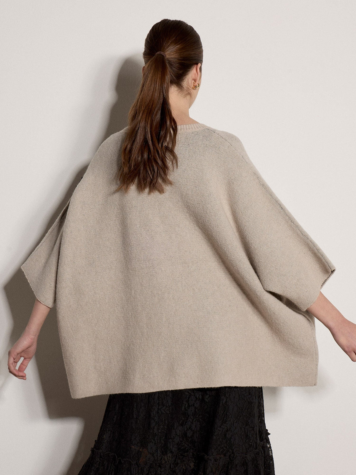 Back view of oversized knit cape jumper with batwing sleeves worn over black lace skirt