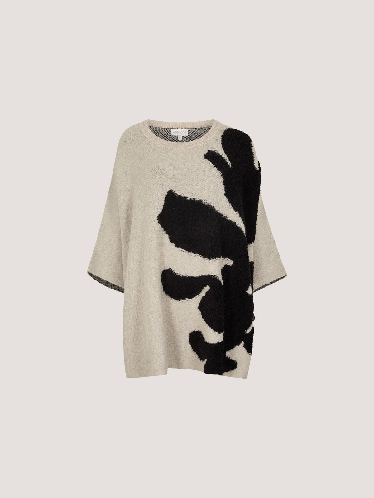 Oversized knit cape jumper with bold abstract black floral intarsia pattern on neutral ground