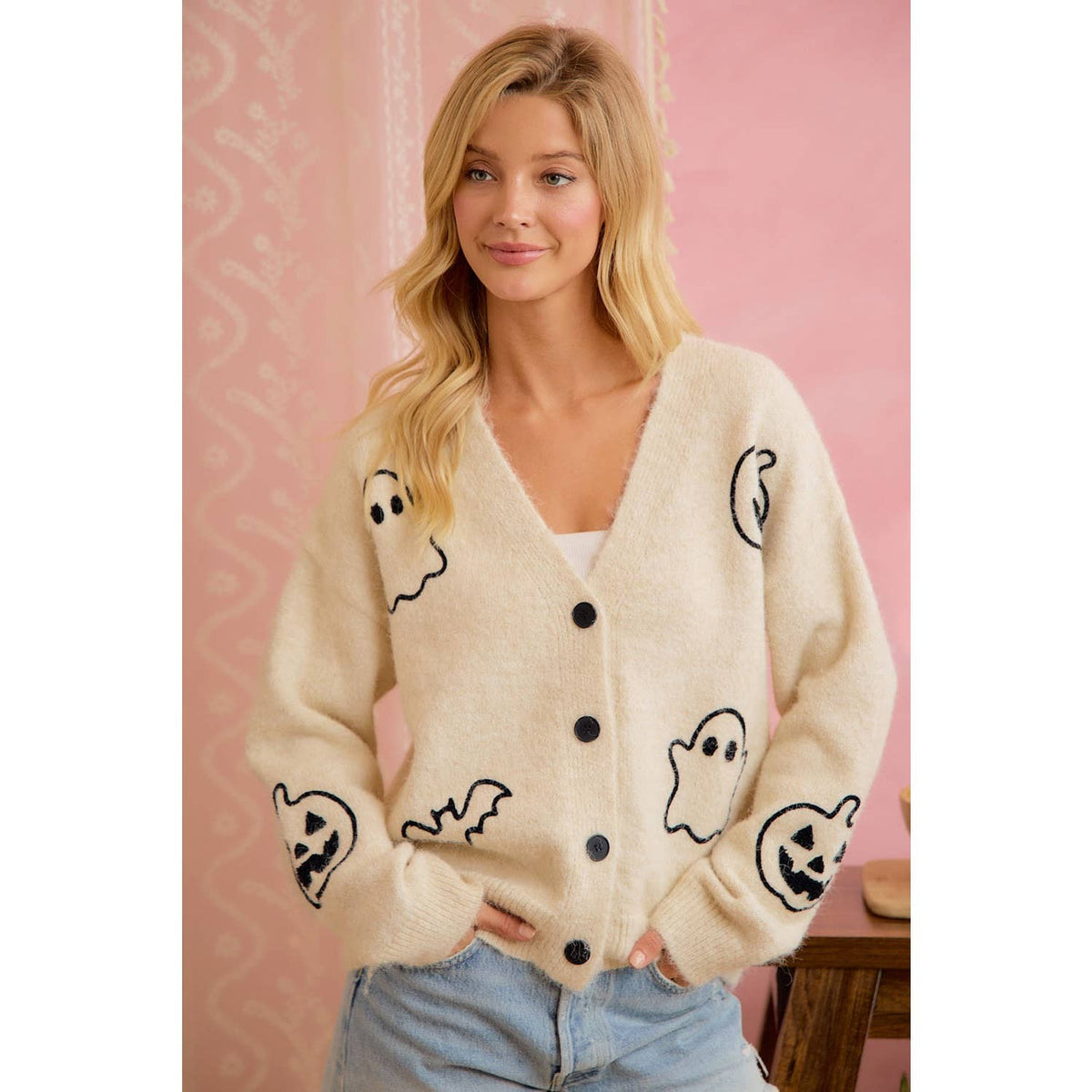 Model wearing ivory button-front cardigan with black ghost, pumpkin, and bat Halloween motifs