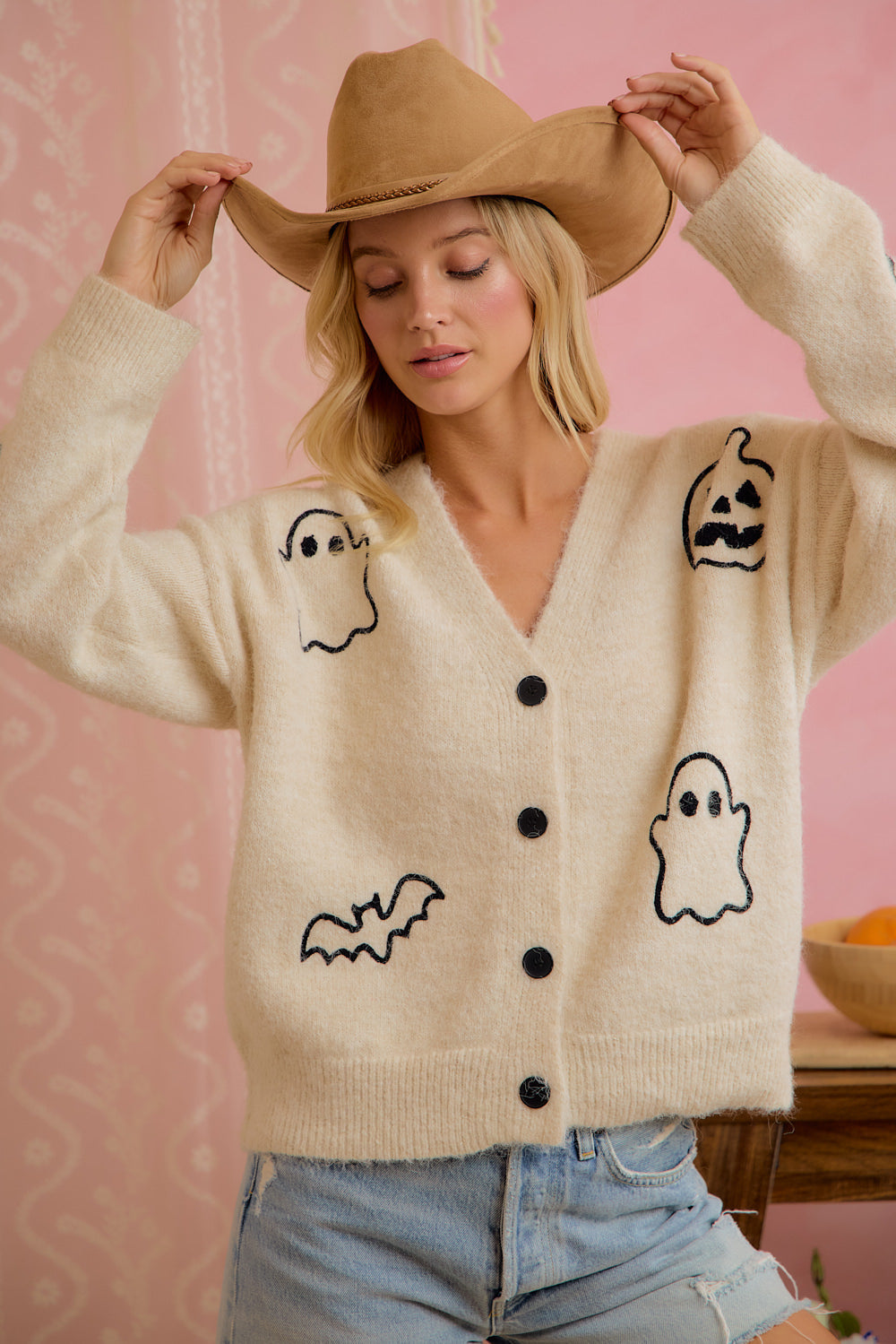 Model wearing ivory button-front cardigan with embroidered Halloween ghost, pumpkin, and bat motifs