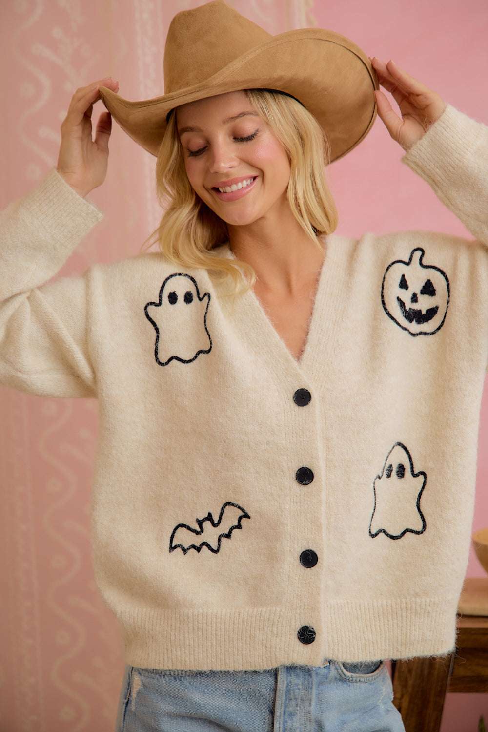 Model wearing ivory button-front cardigan with embroidered Halloween ghost, pumpkin, and bat motifs