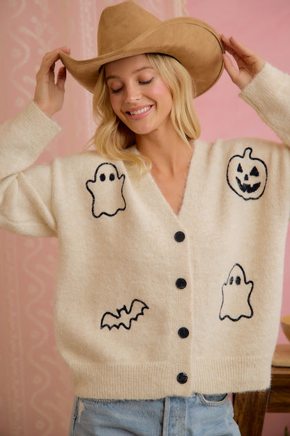 Model wearing ivory button-front cardigan with embroidered Halloween ghost, pumpkin, and bat motifs