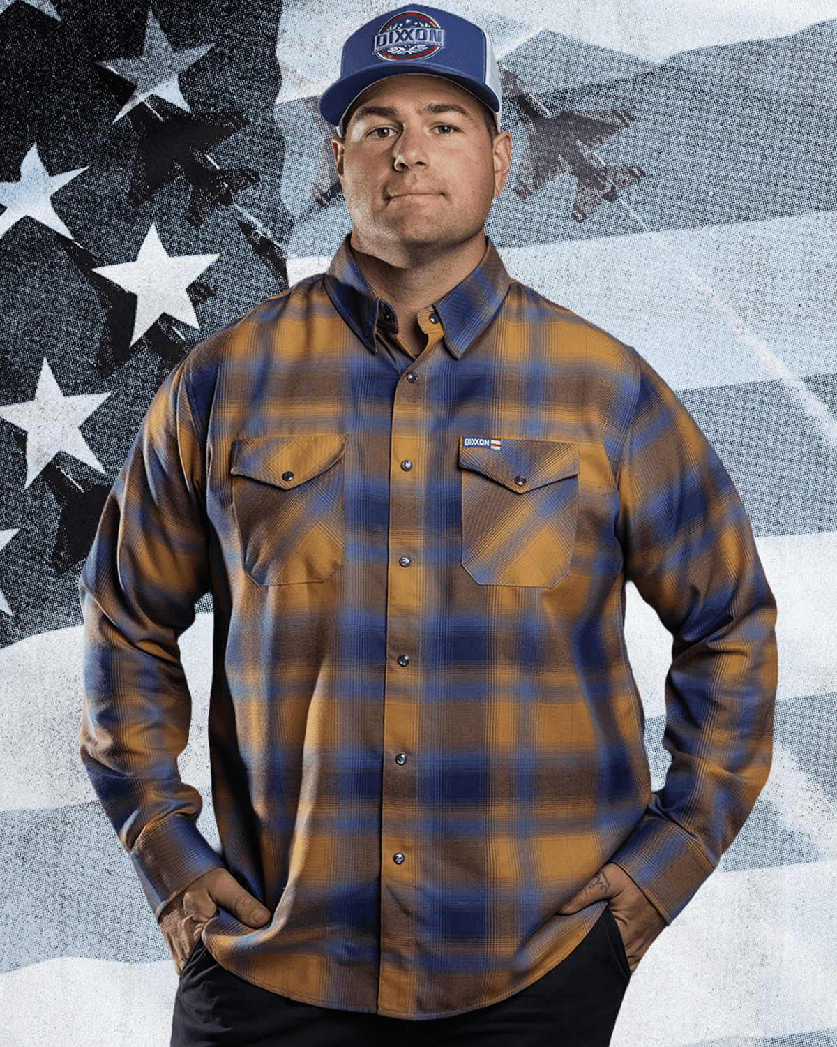 Man wearing Dixxon gold and navy plaid flannel shirt with matching branded cap, hands on hips