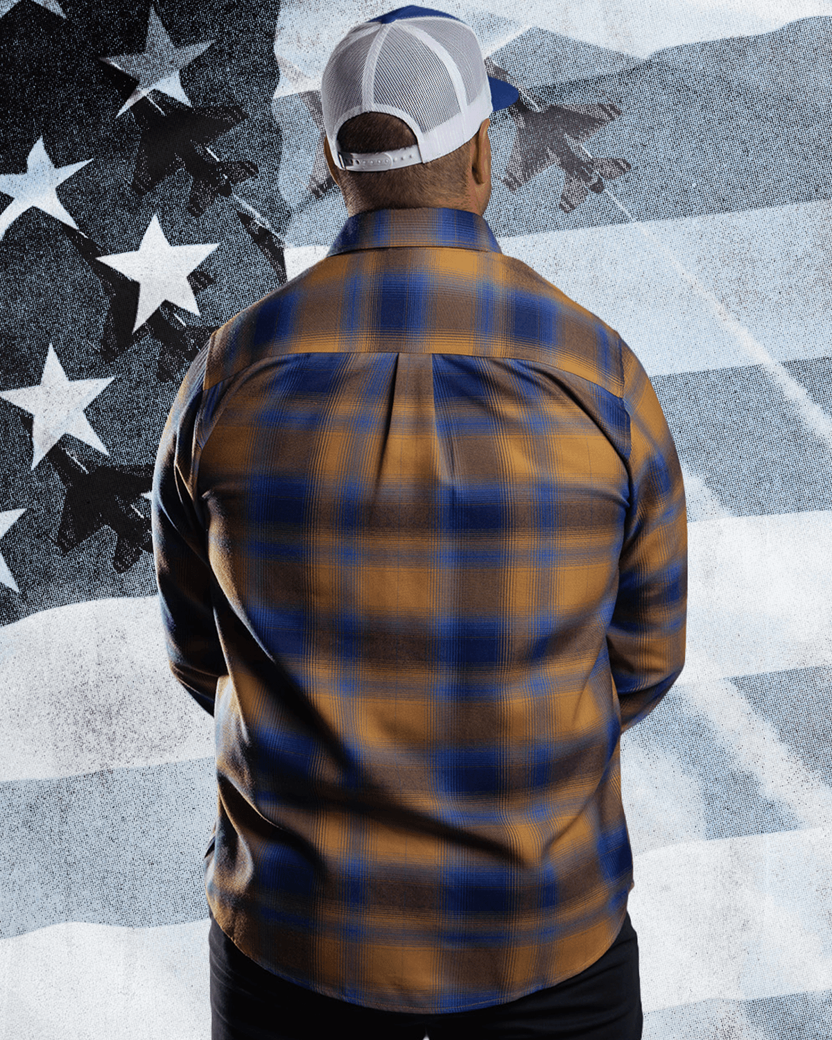 Back view of men's gold and blue plaid flannel shirt with white trucker hat against American flag backdrop