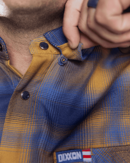 Close-up detail of Dixxon flannel shirt collar with snap buttons in blue and gold plaid pattern