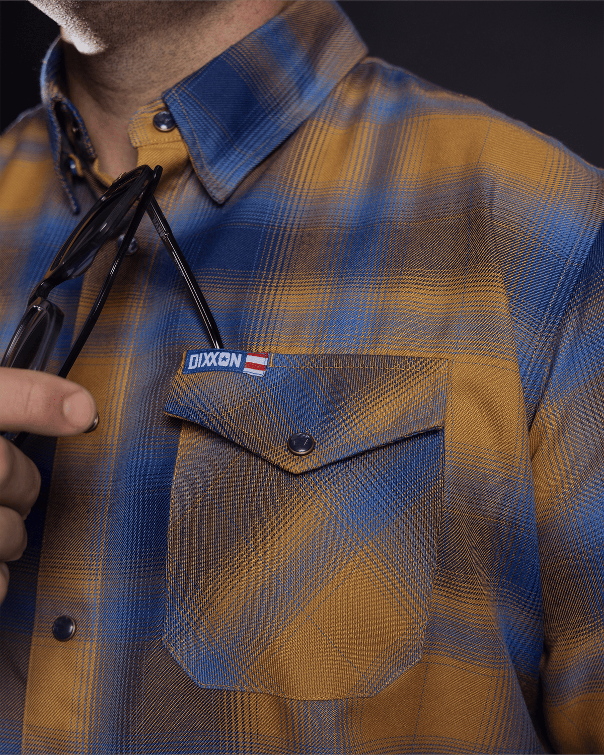 Close-up detail of Dixxon flannel chest pocket with snap button and brand label patch