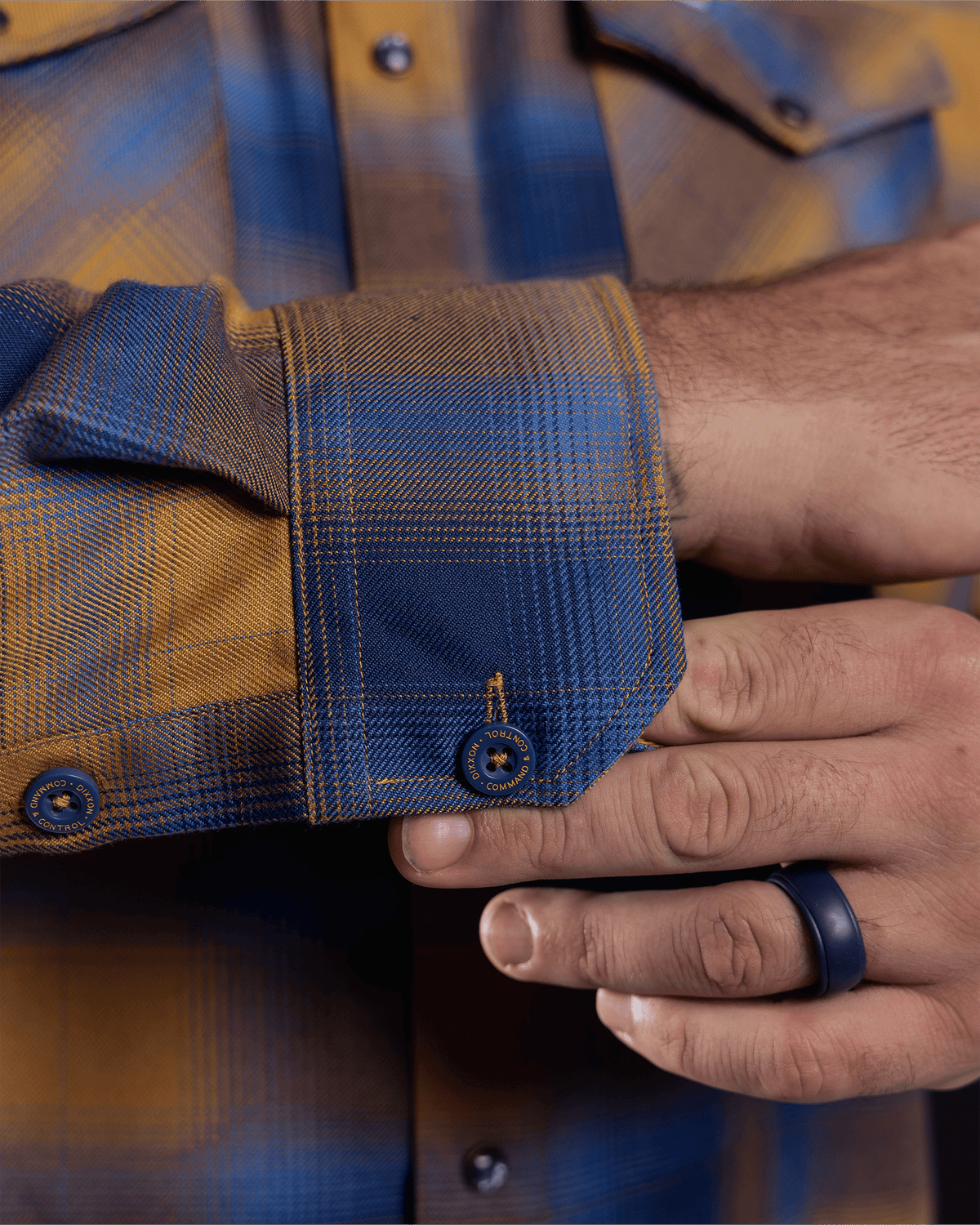Close-up detail of flannel shirt cuff with branded navy buttons and plaid pattern
