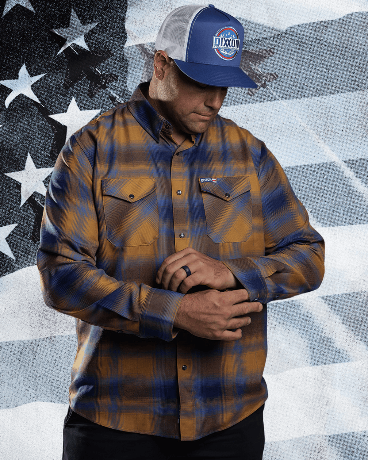 Man adjusting cuffs of a plaid flannel shirt wearing a Dixxon trucker hat