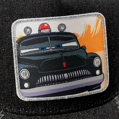 Close-up detail of embroidered patch on black cap featuring Sheriff car from Pixar Cars